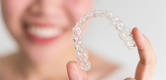 woman smiling holding clear orthodontic aligner